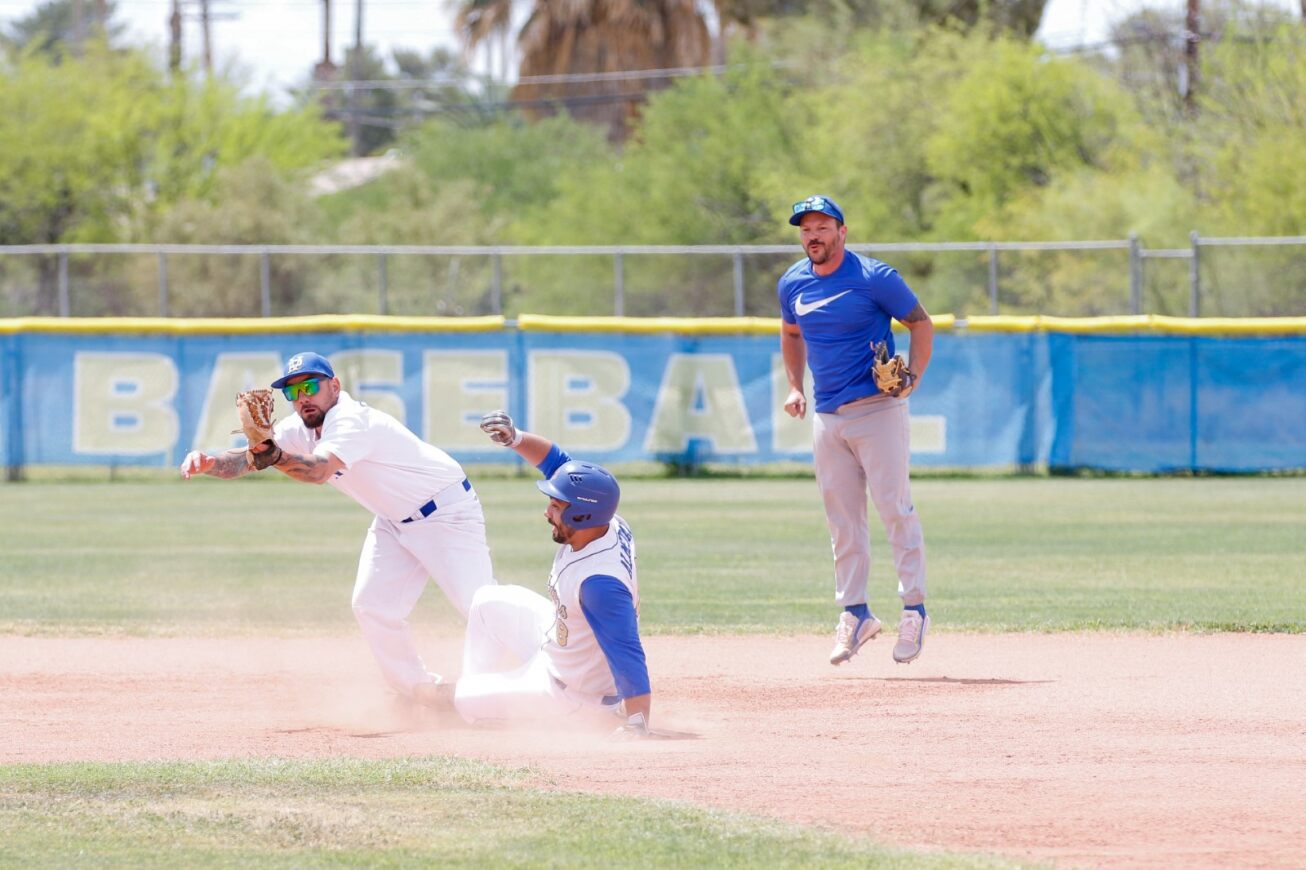An alumni player slides into the base while another player lunges to catch the baseball