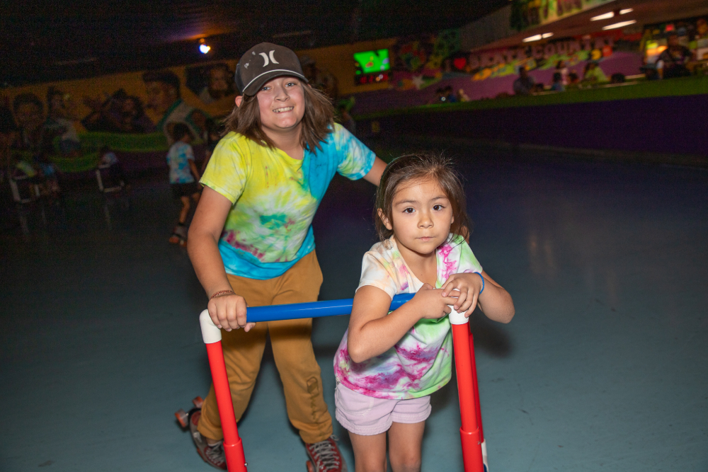 A boy in a tie-dye shirt pushes a little girl with her skating walker
