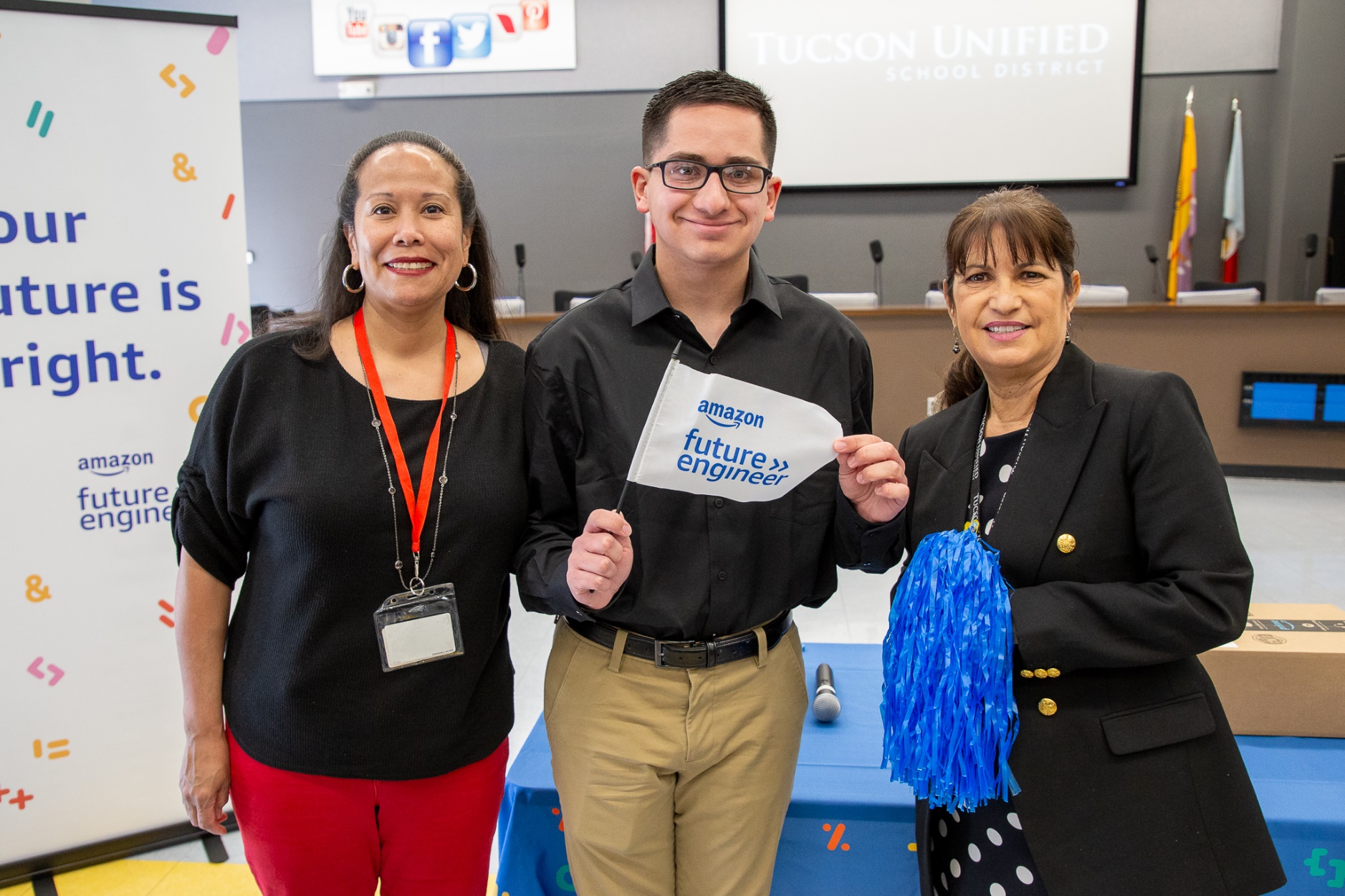 Tucson High student Anthony Talavera holds up an Amazon Future Engineer flag and poses with two staff members.