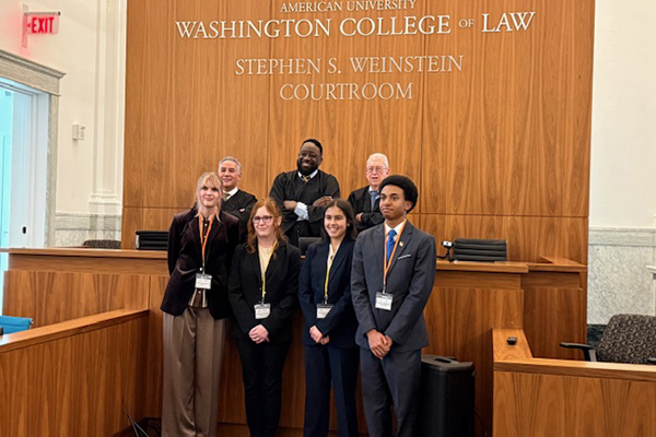 A group of high school students pose in a courtroom in front of a panel of judges