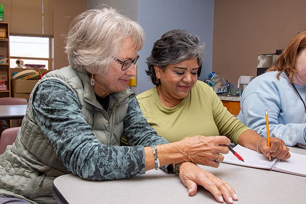 Two women sit at a table while working on a worksheet