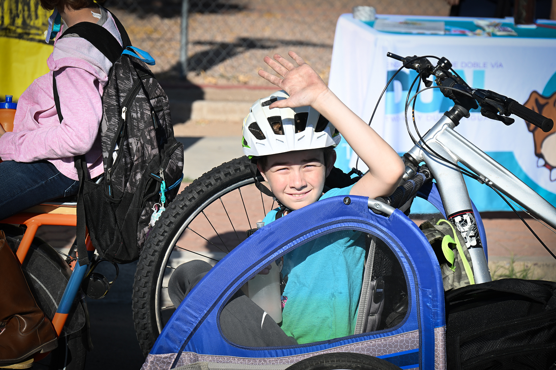 A boy in a bike helmet waves from his bike carrier