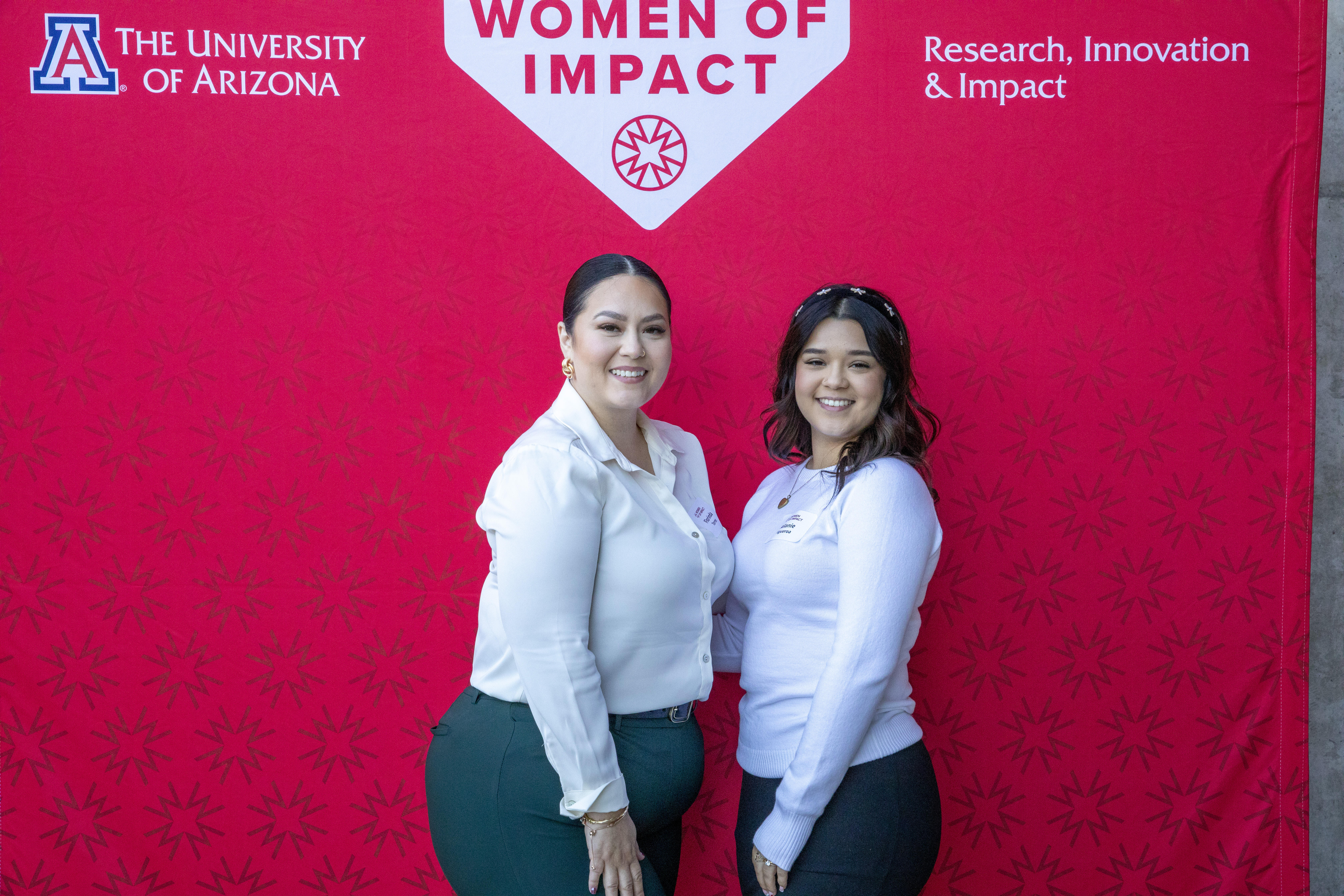 A teen girl smiles with her mentor in front of a red Young Women of Impact Banner