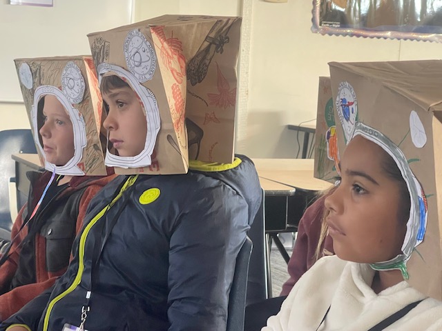 First and second graders wearing their paper bag astronaut helmet that they made.