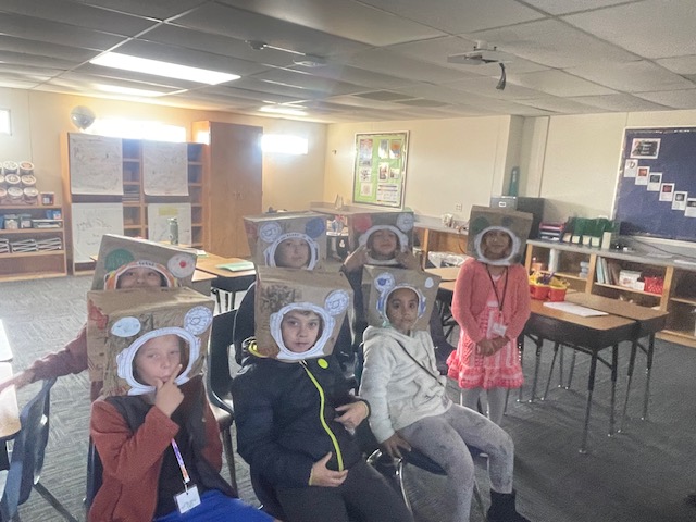 First and second graders wearing their paper bag astronaut helmet that they made.