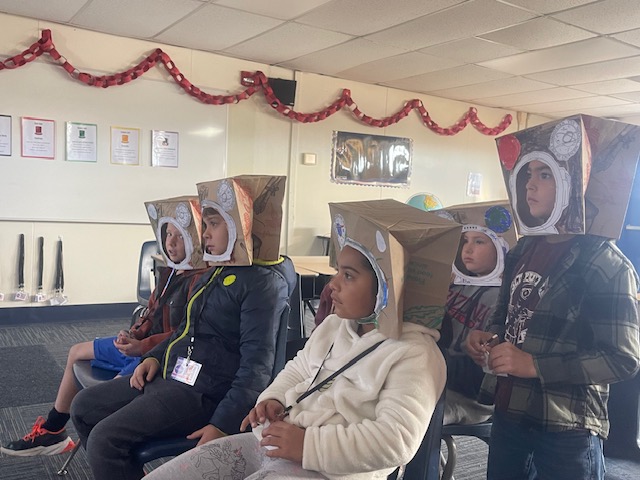 First and second graders wearing their paper bag astronaut helmet that they made.