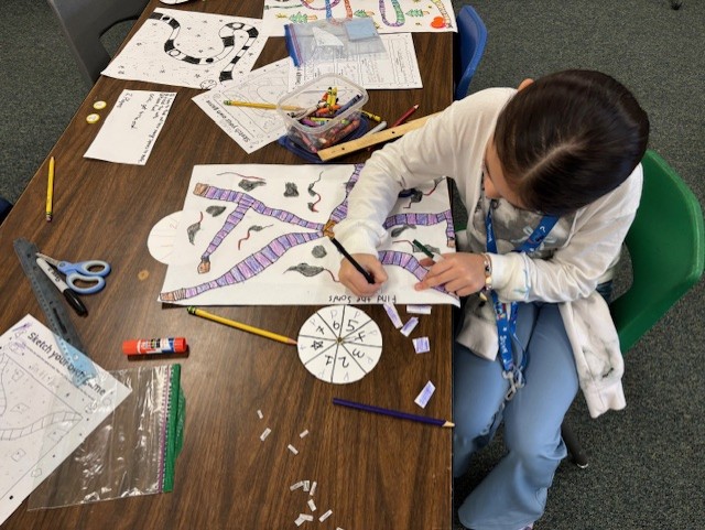 This image shows a student or students creating a board game as part of  the GATE program's GAME Design Unit.