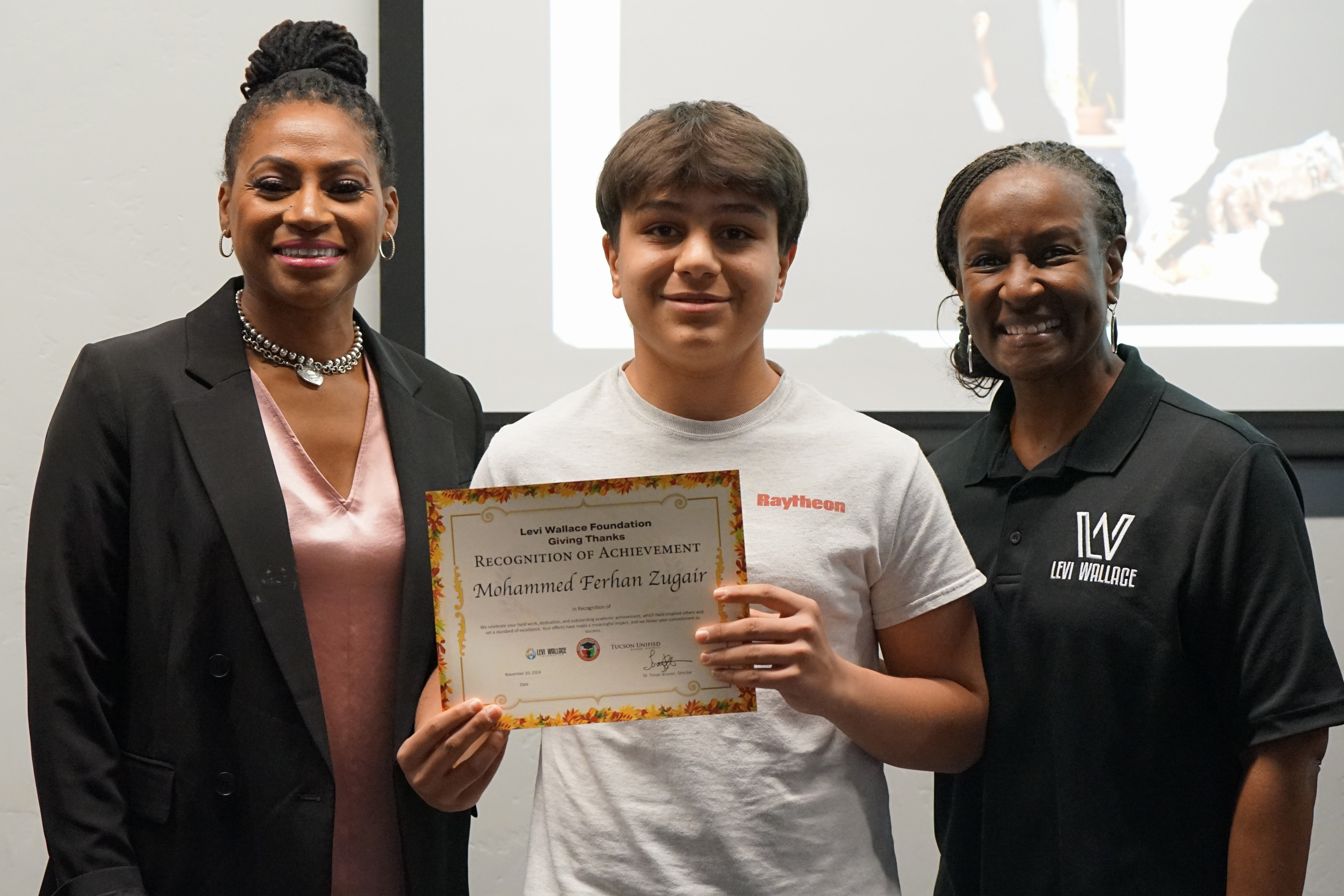 A young man holds a certificate in between two women