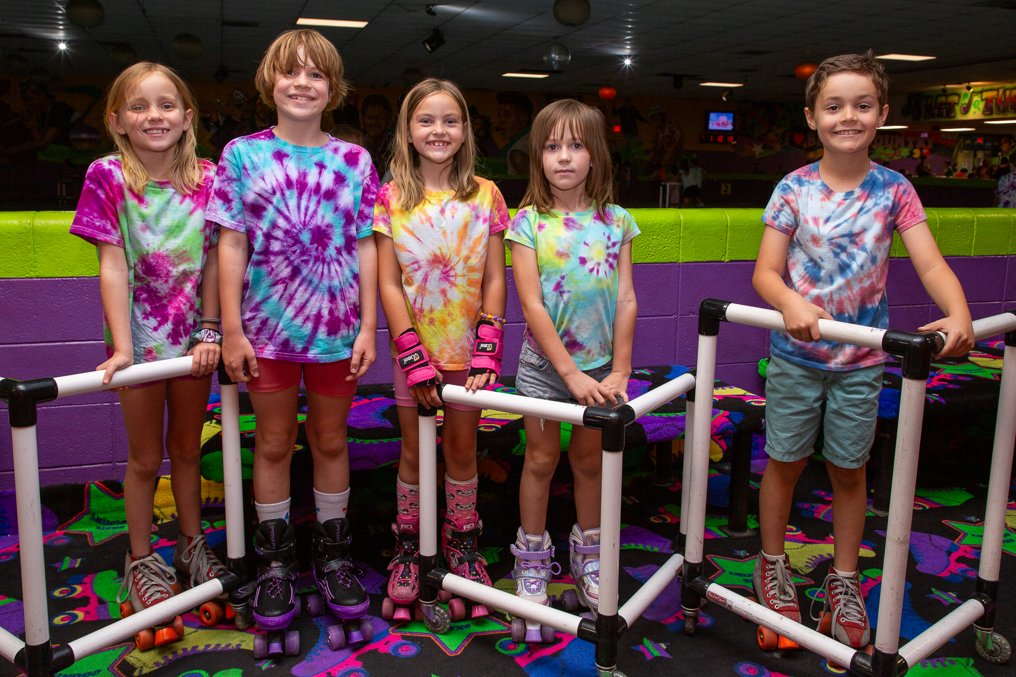 Five kids in tie-dye shirts smile for a photo after rollerskating
