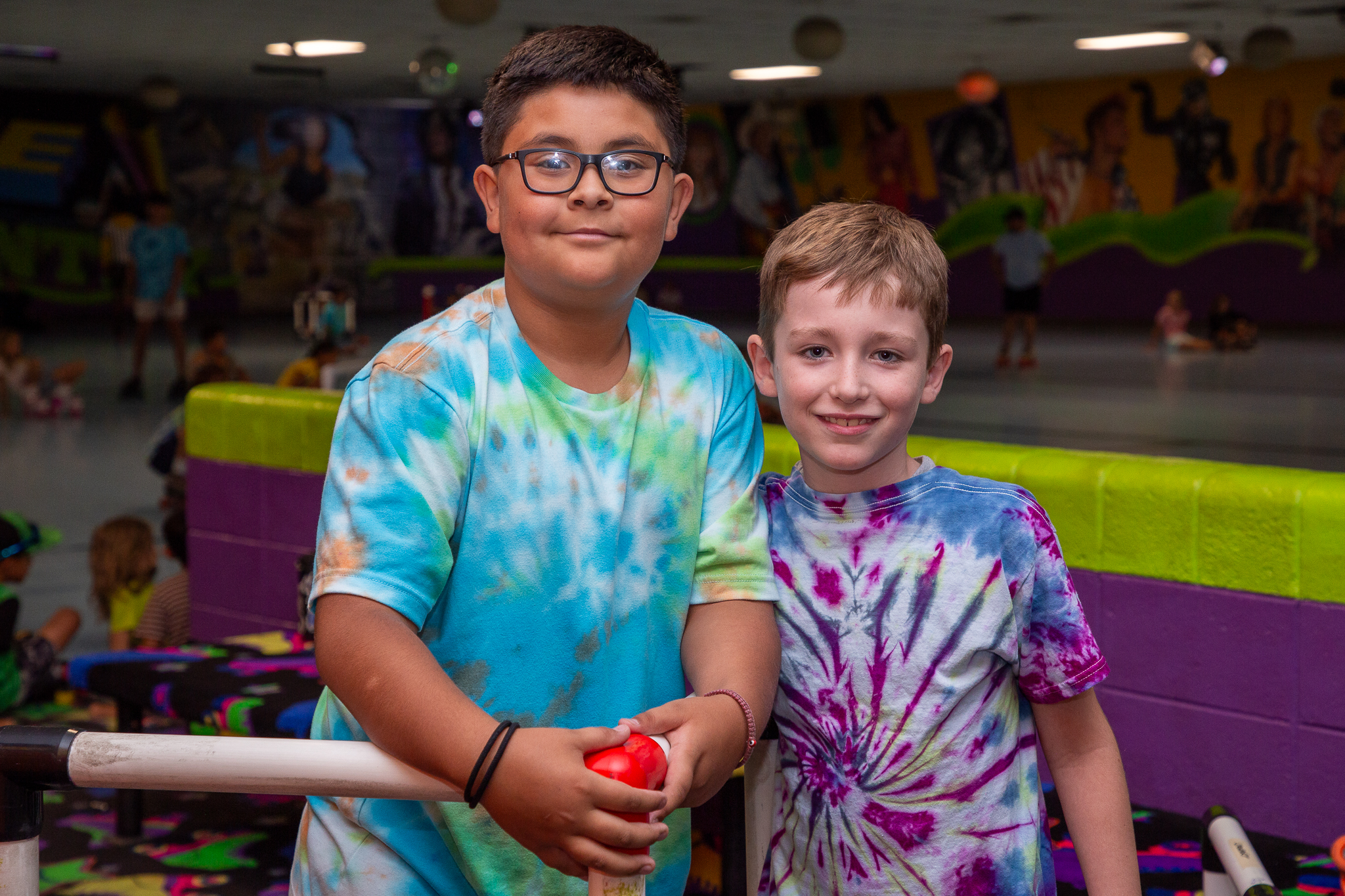 Two boys in tie-dye shirts smile at the roller skating rink