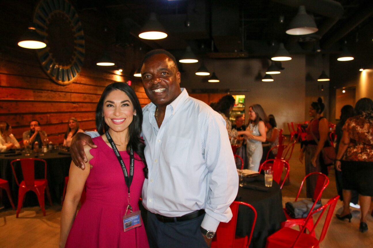 A woman with dark hair and a pink dress and an African American man in a white shirt smile and pose for a photo