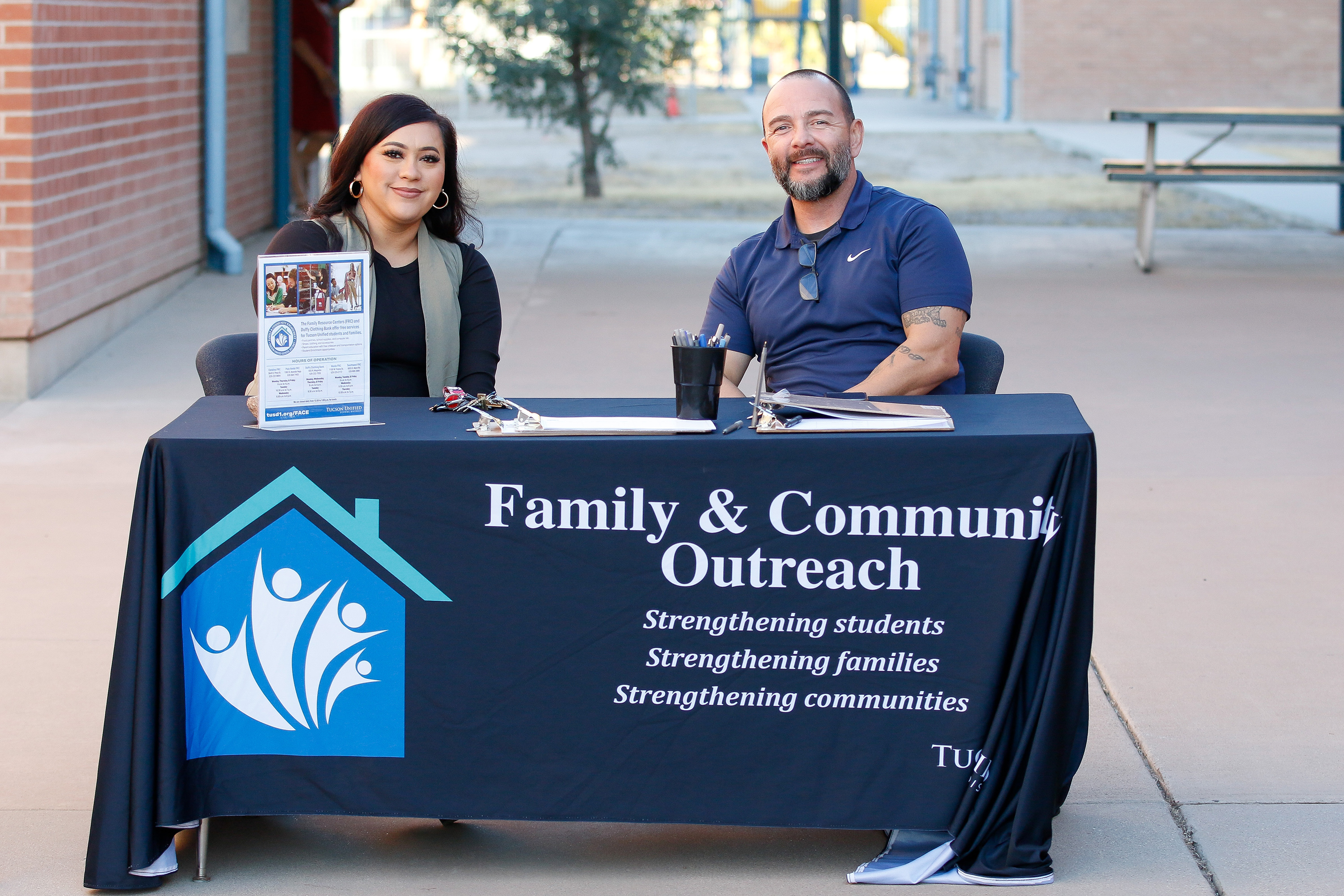 A woman and a man smile at a table with a tablecloth reading Family and Community Outreach