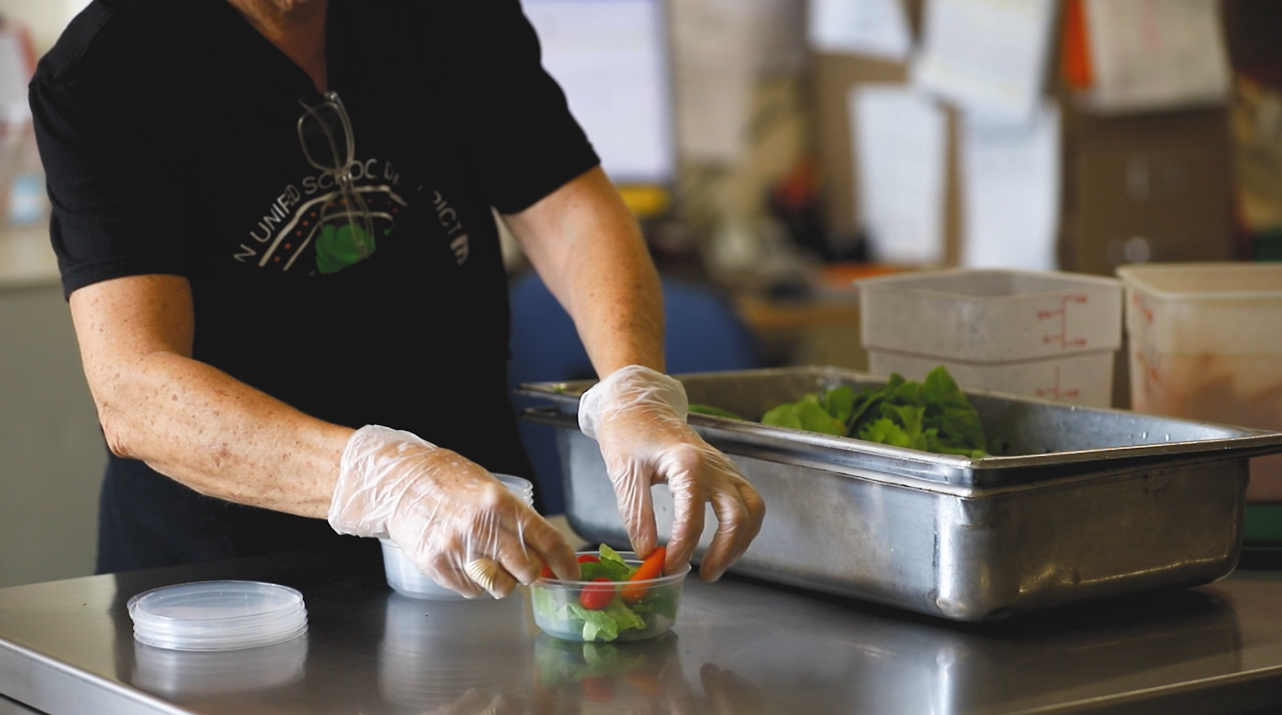 Closeup of a Food Services worker's hands putting together a salad bowl