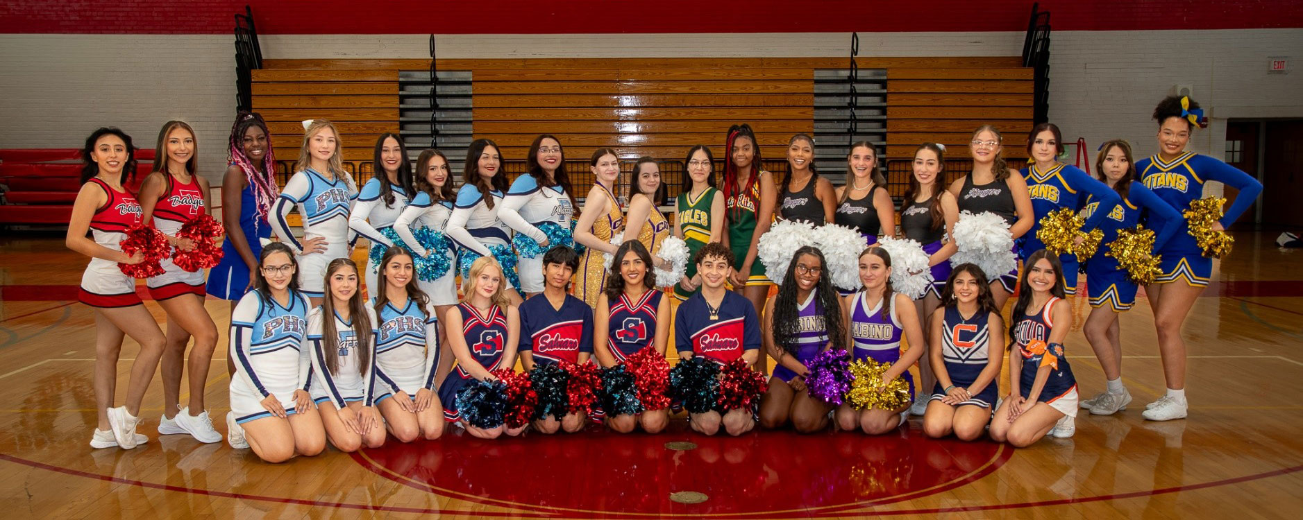 Cheerleader from all Tucson Unified High Schools pose for a photo in a gym.