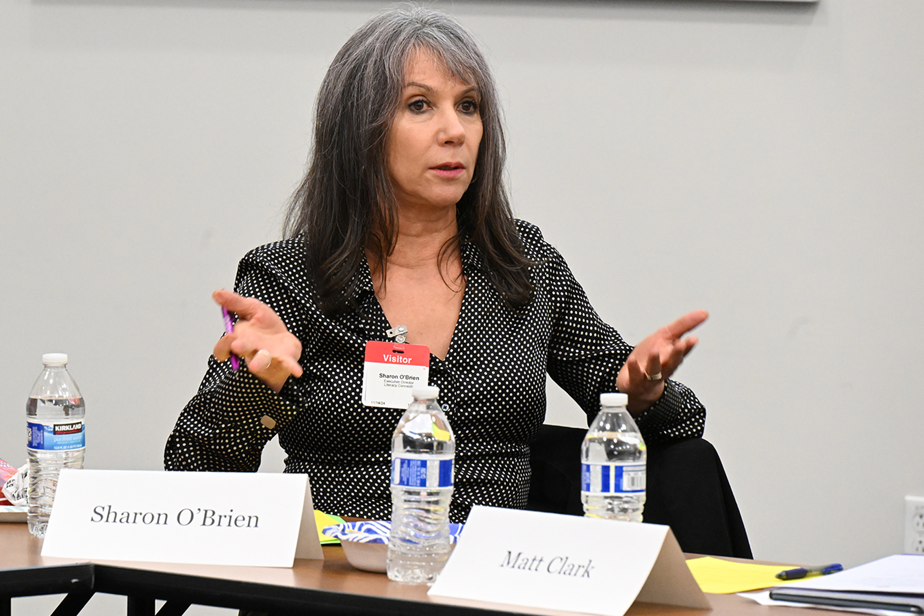 A women with gray hair and a black polka dot blouse gestures with her hands