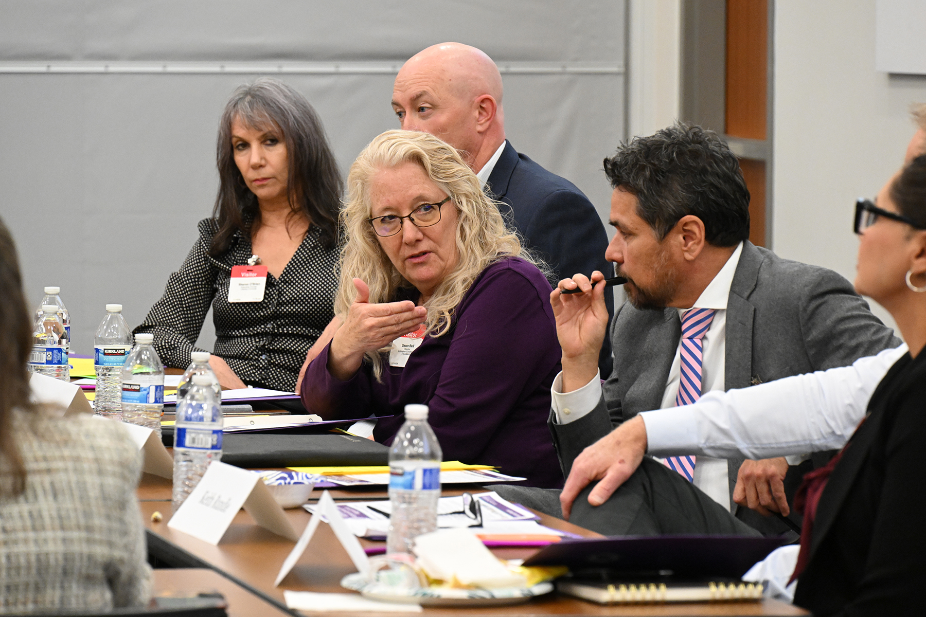 A woman with blonde hair and a purple top talks while other leaders listen