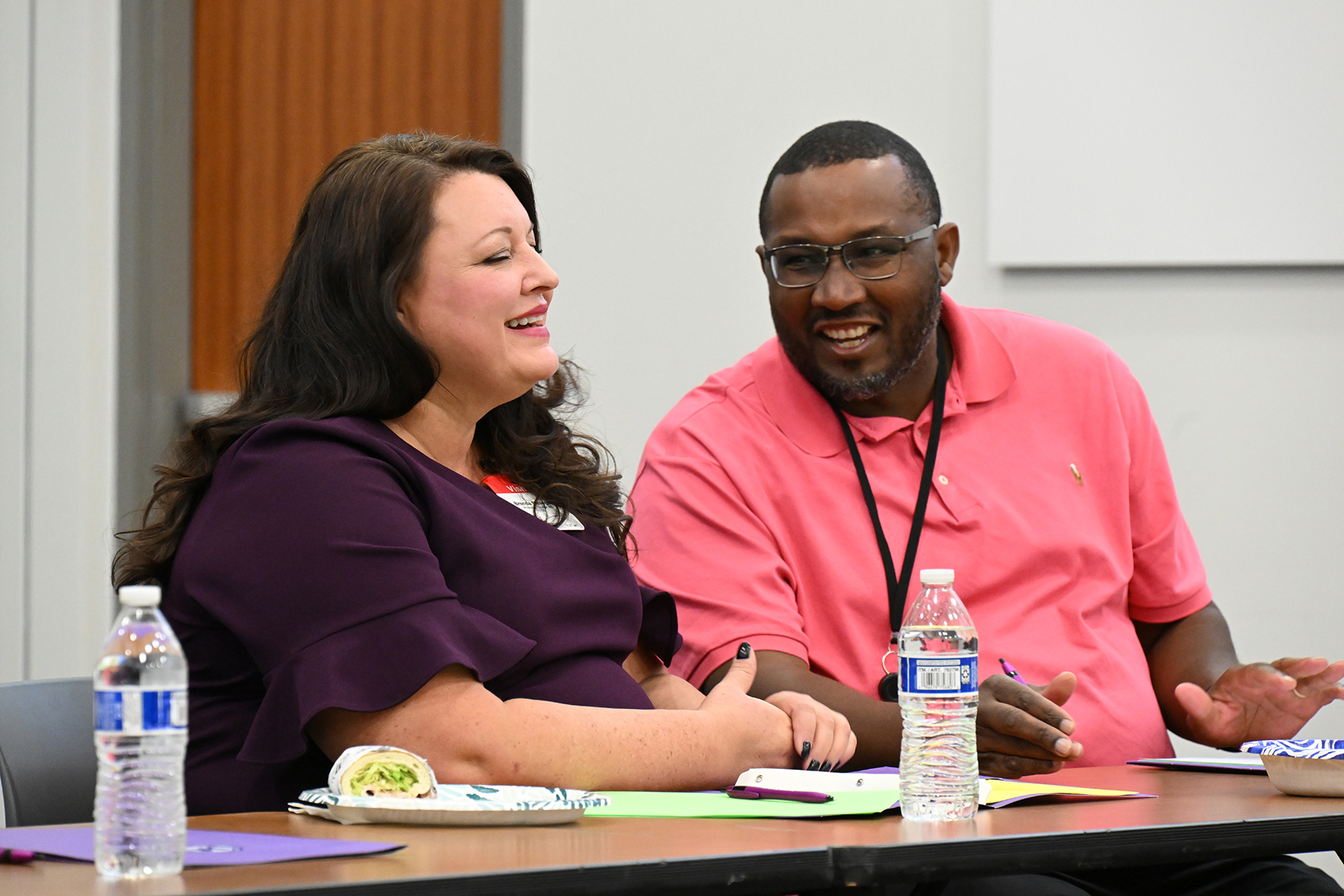 A woman in a purple top and a man in a pink shirt laugh together