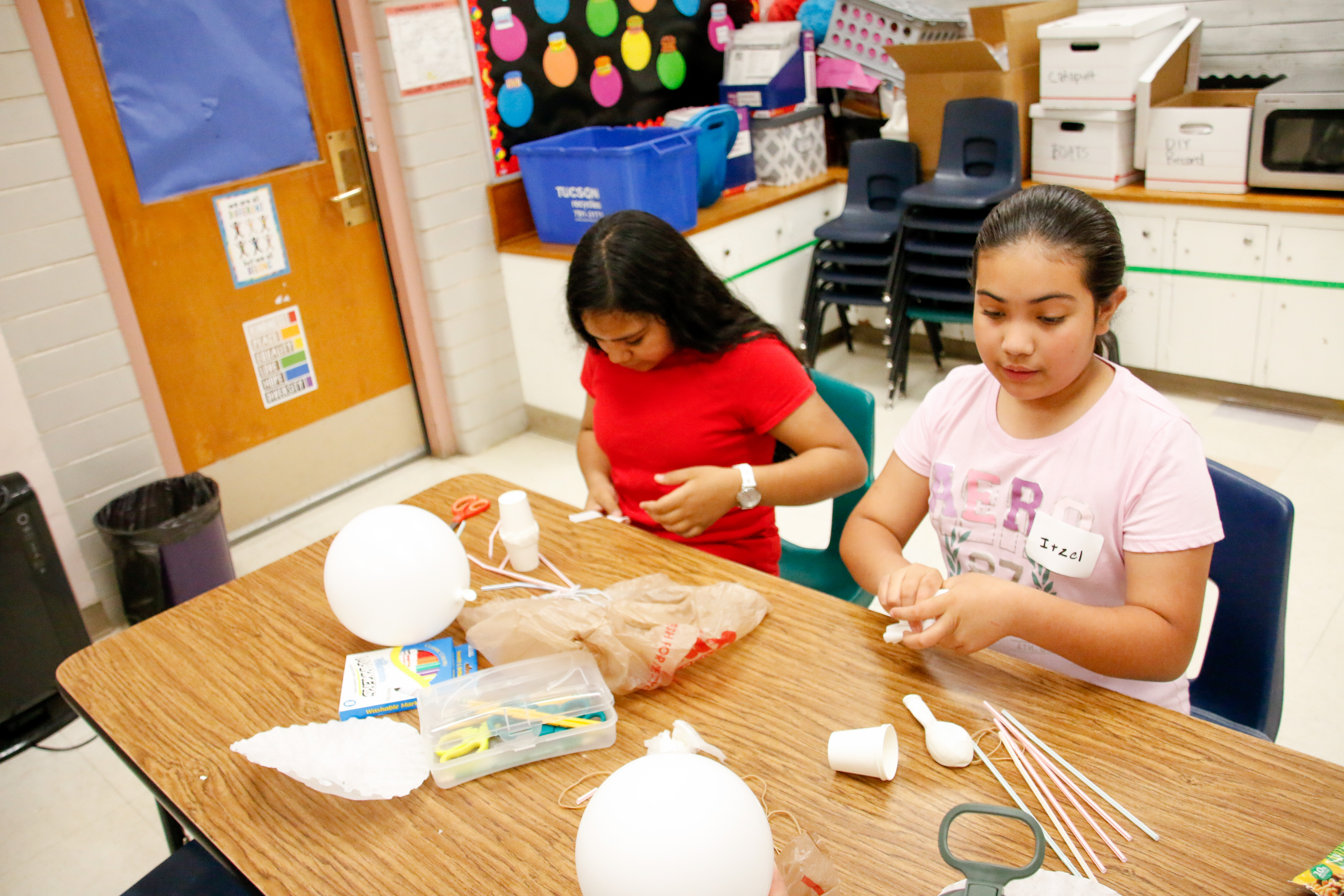 Two girls with dark brown hair work on creating a contraption to drop an egg