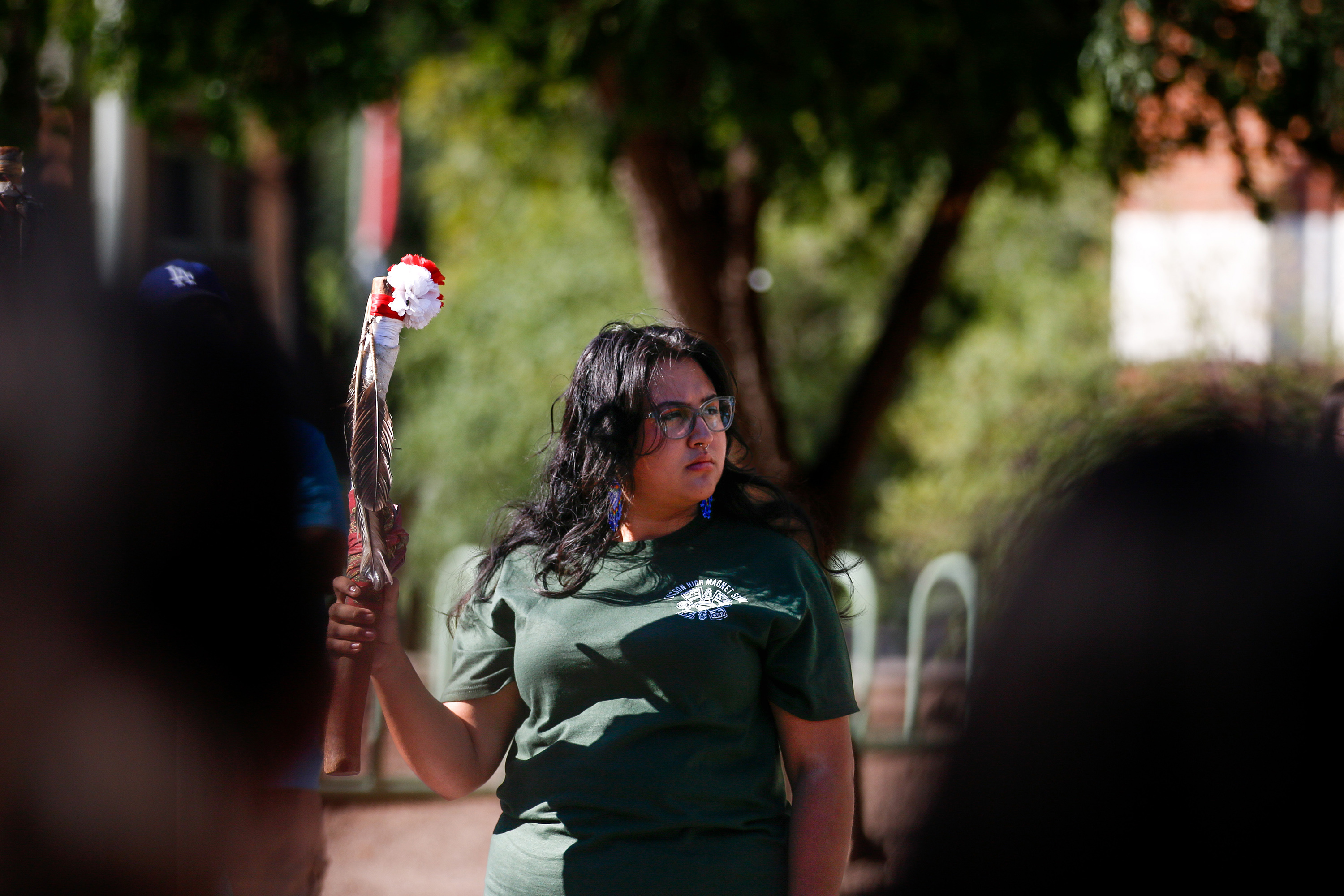 A woman holds up a decorated stick with a feather.