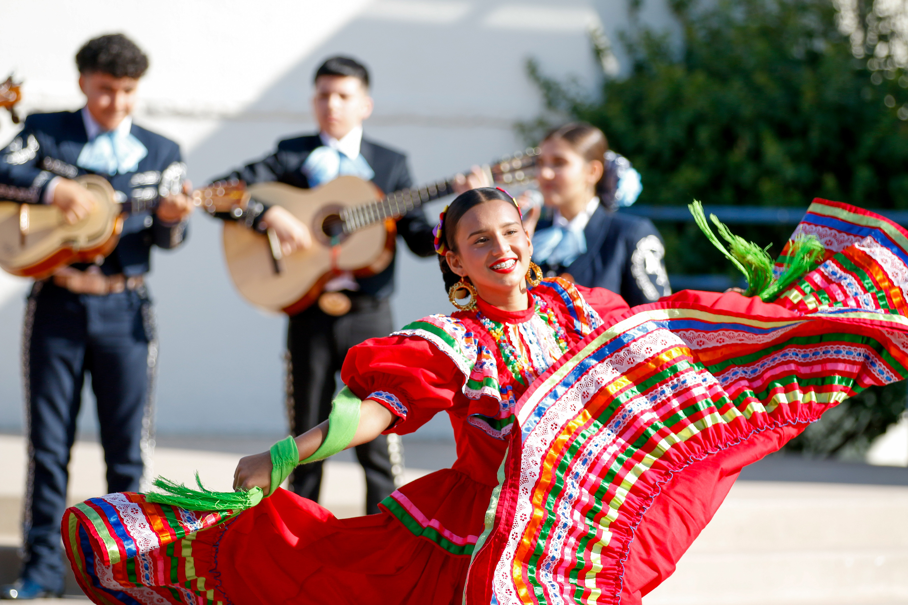 A folklorico dancer smiles and twirls in her red dress as the mariachi performs