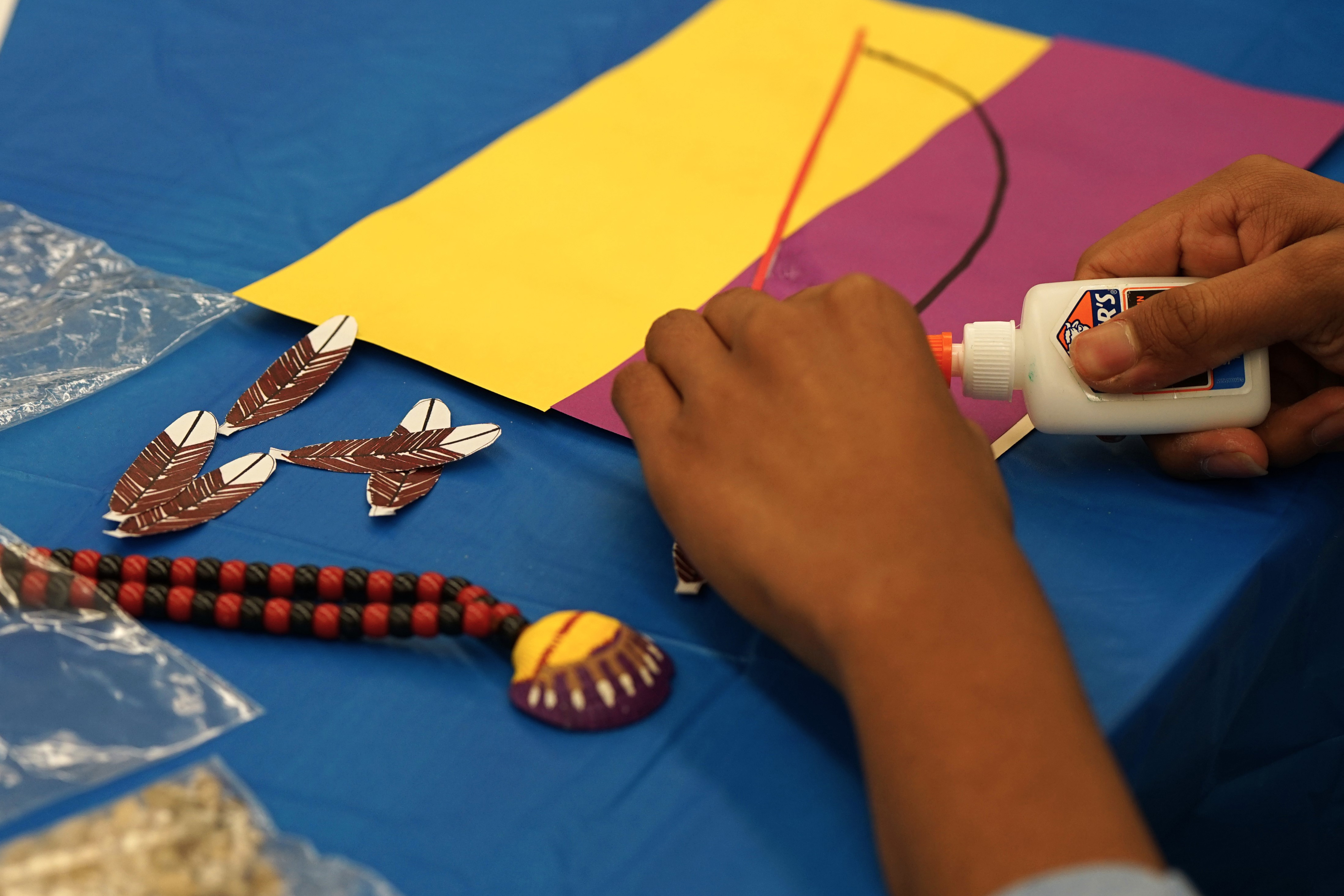 A student works on gluing a craft project with beads and feathers