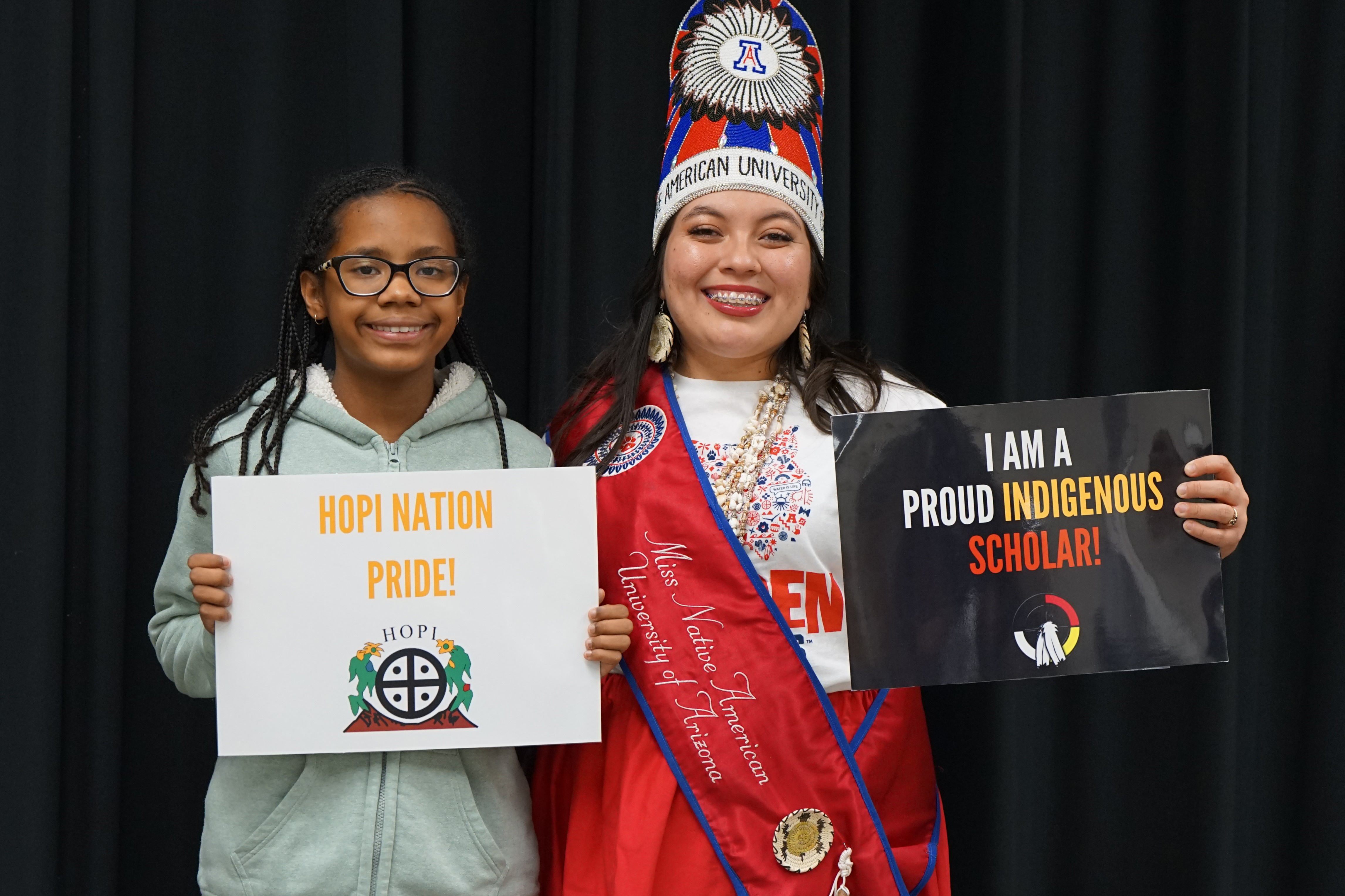 Two girls hold up signs reading Hopi Nation Pride! and I Am a Proud Indigenous Scholar!