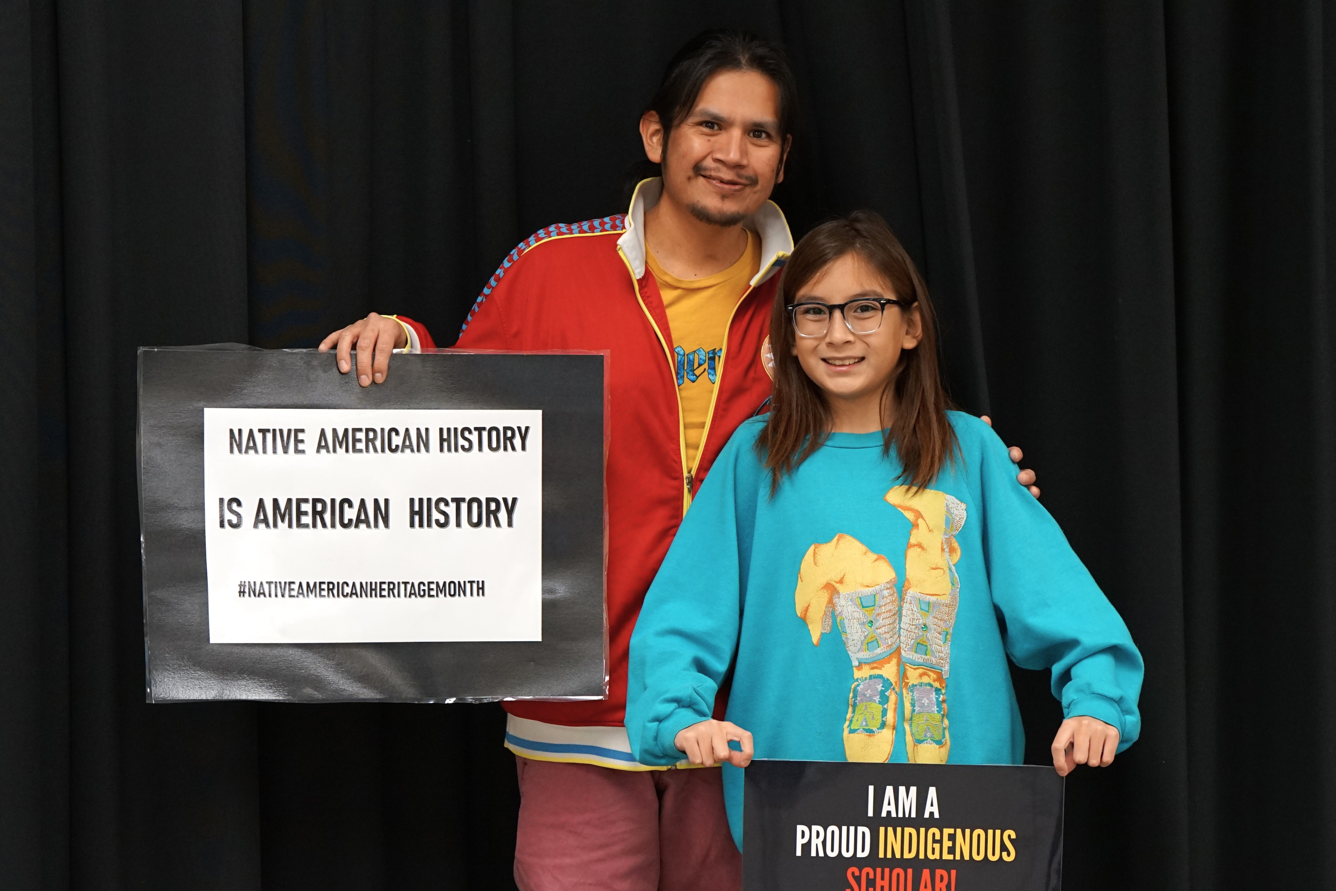 Two students hold up signs reading Native American History is American History and I am a Proud Indigenous Scholar!