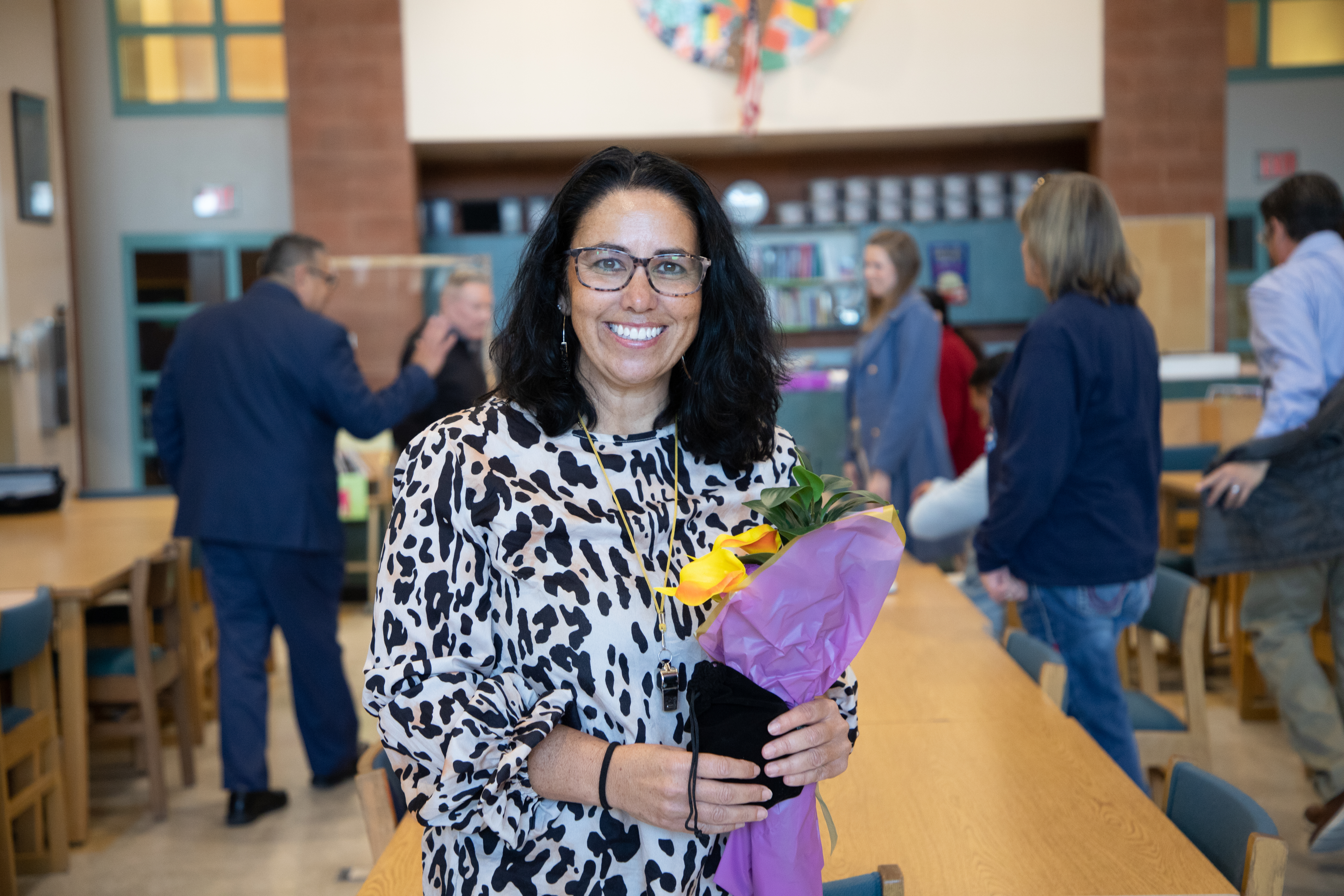 A woman with dark hair and glasses smiles with a bouquet of flowers