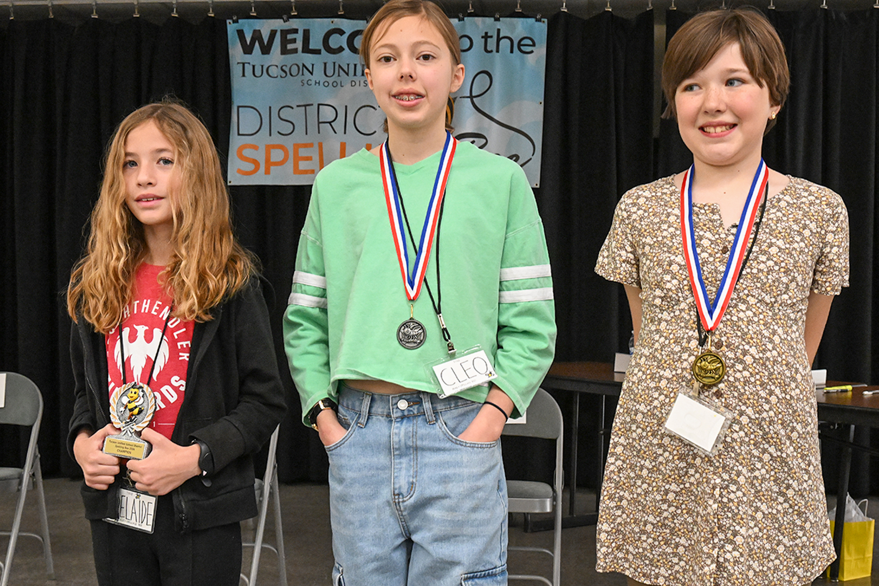 Three young girls stand smiling after being awarded best spellers at the District Spelling Bee