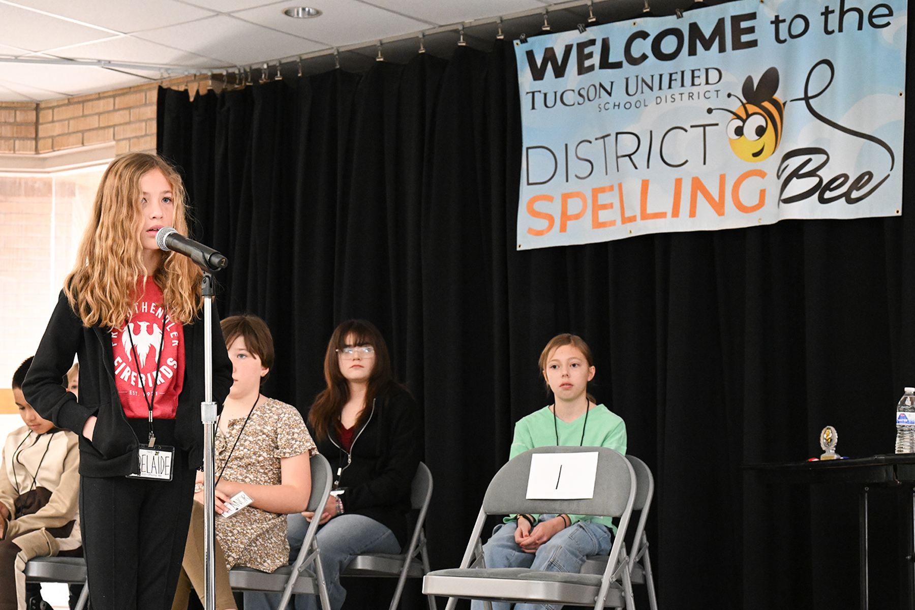 A young girl stands at the microphone preparing to spell her word