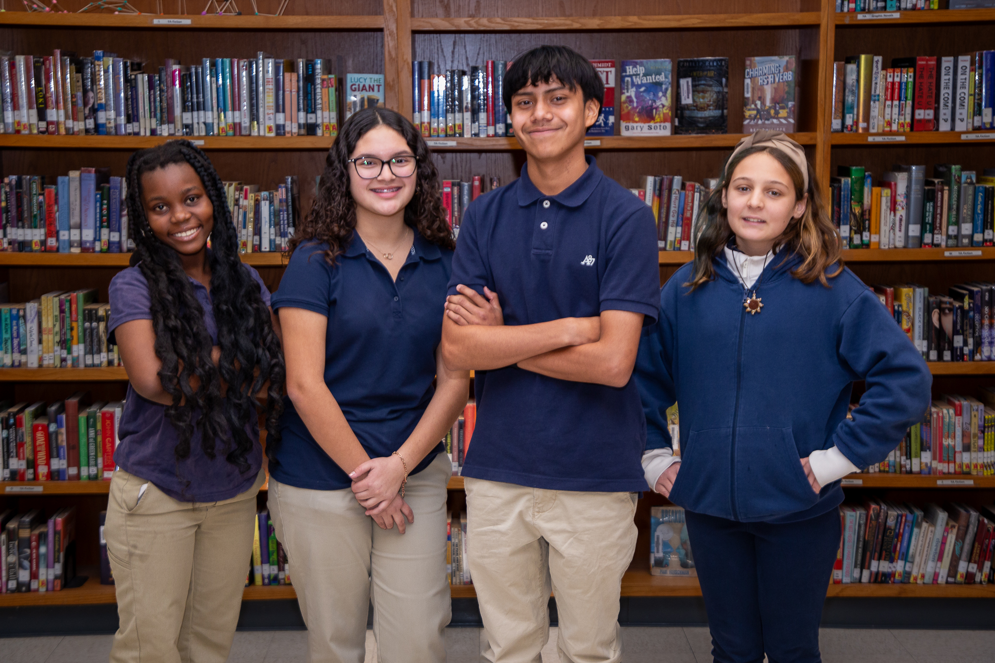 Four students smile in front of bookshelves in the library