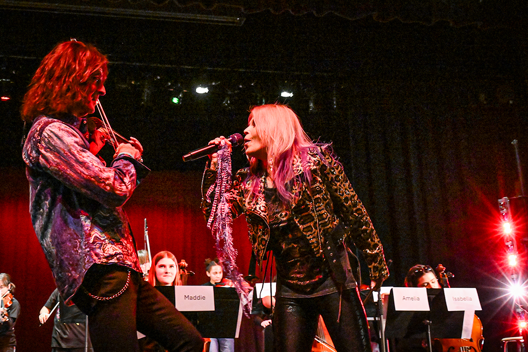 Mark Wood plays violin while Laura Kaye sings at him on stage with students behind them