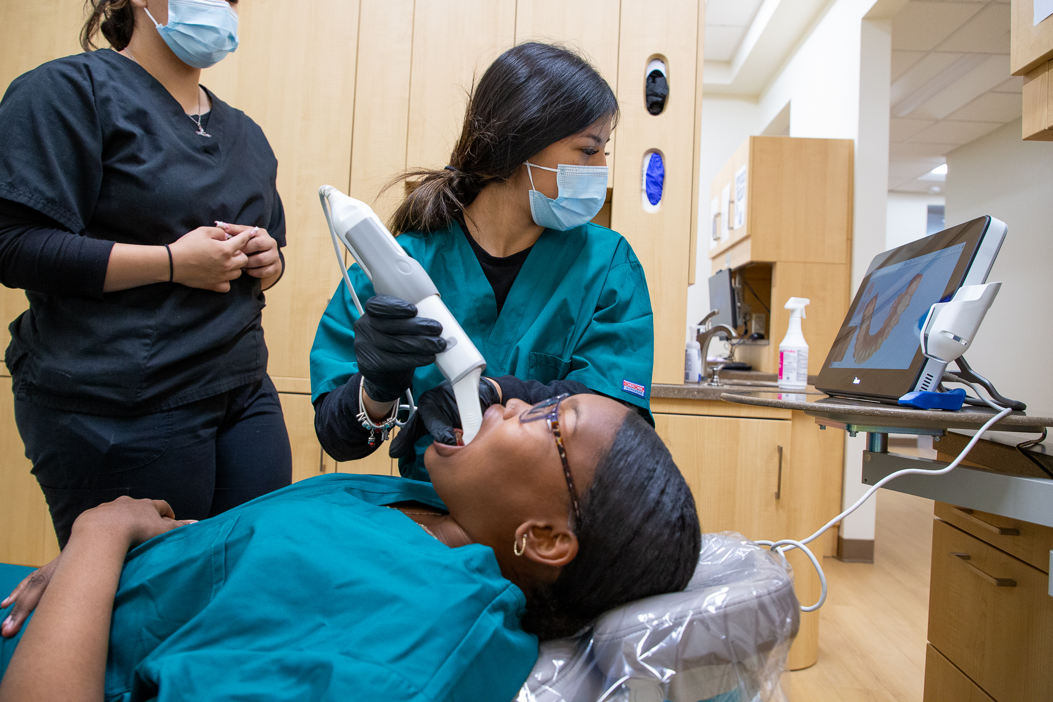A dental assisting student performs a scan on another student as her instructor observes